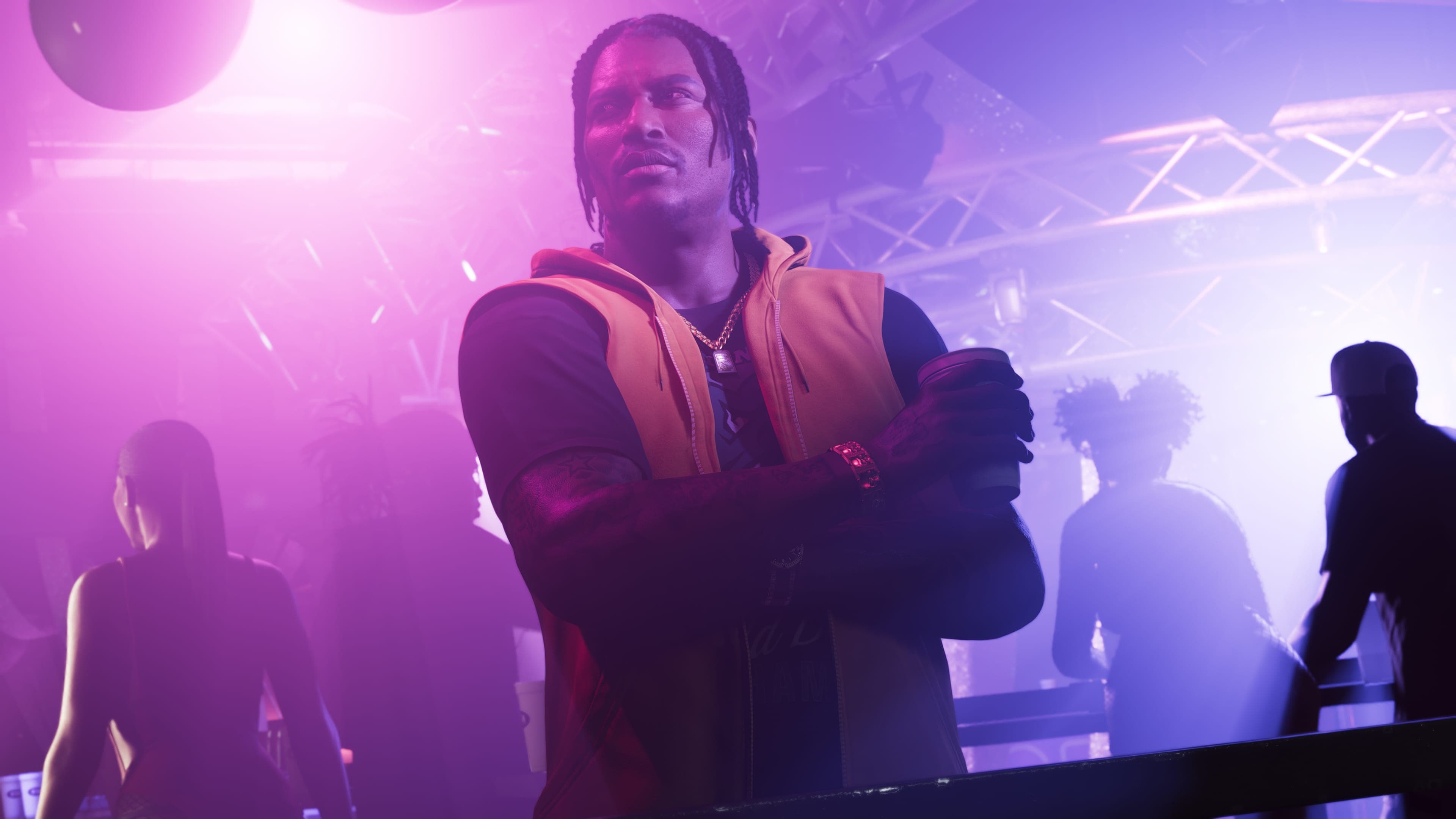 Dre’Quan Priest in an orange vest crosses his arms with a drink in hand under purple club lights