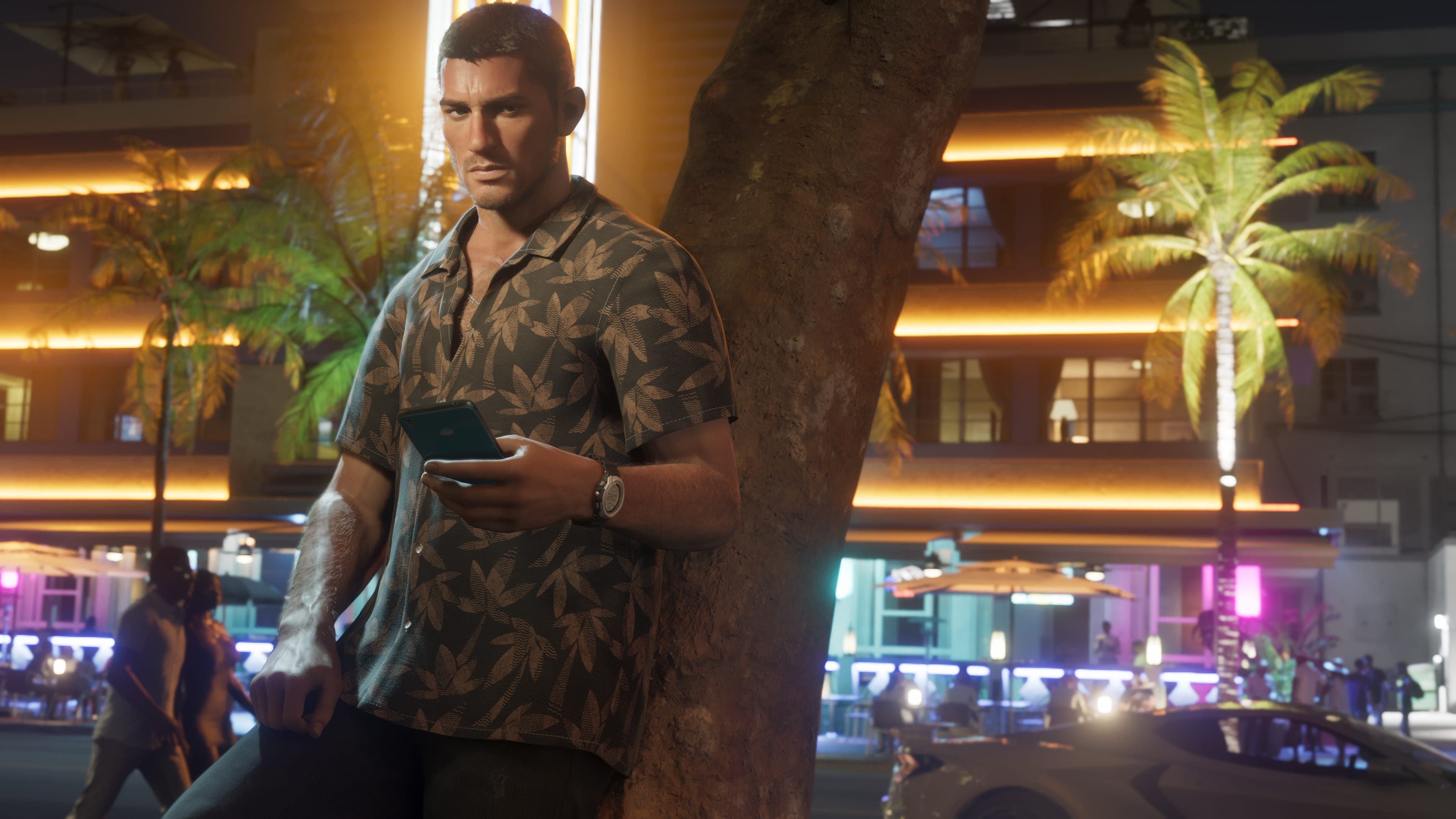 Jason Duval in a leaf-print shirt leans on a tree and checks his phone outside neon-lit hotels at night