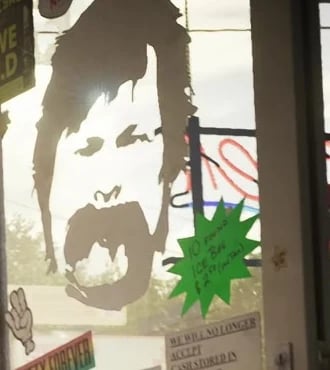 Calcomanía de un rostro sin identificar en la puerta de la licorería del Tráiler 1 oficial; su identidad como Everett Morgan está sin confirmar